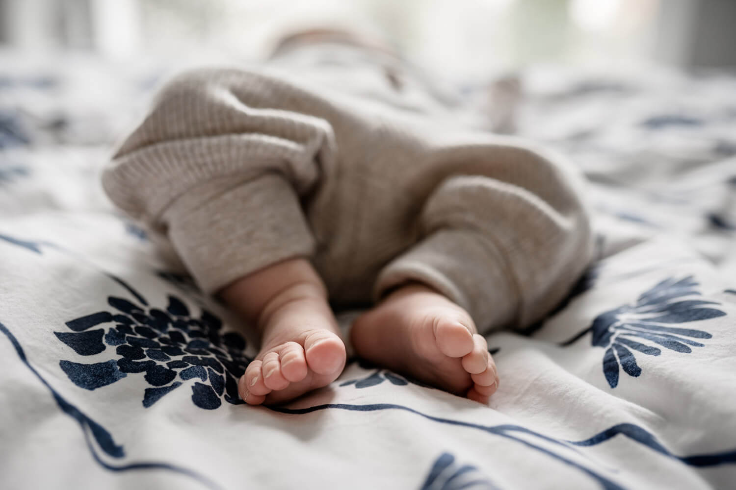 Nahaufnahme Babyfüße auf Elternbett, gemusterte Bettwäsche mit blauen Blümchen