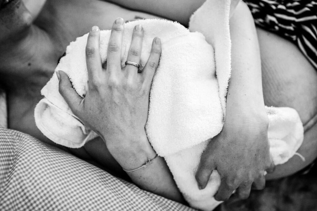 Nahaufnahme Mutter hält ihr gerade geborenes Baby in Handtuch gewickelt im Arm, Geburtsfotografie im Geburtshaus Hannove