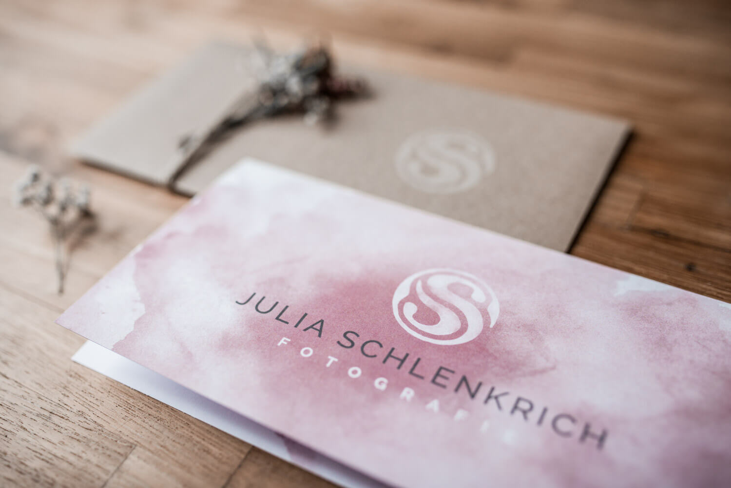 Rosa gestalteter Faltgutschein von Julia Schlenkrich Fotografie liegt auf Holztisch mit Trockenblumen