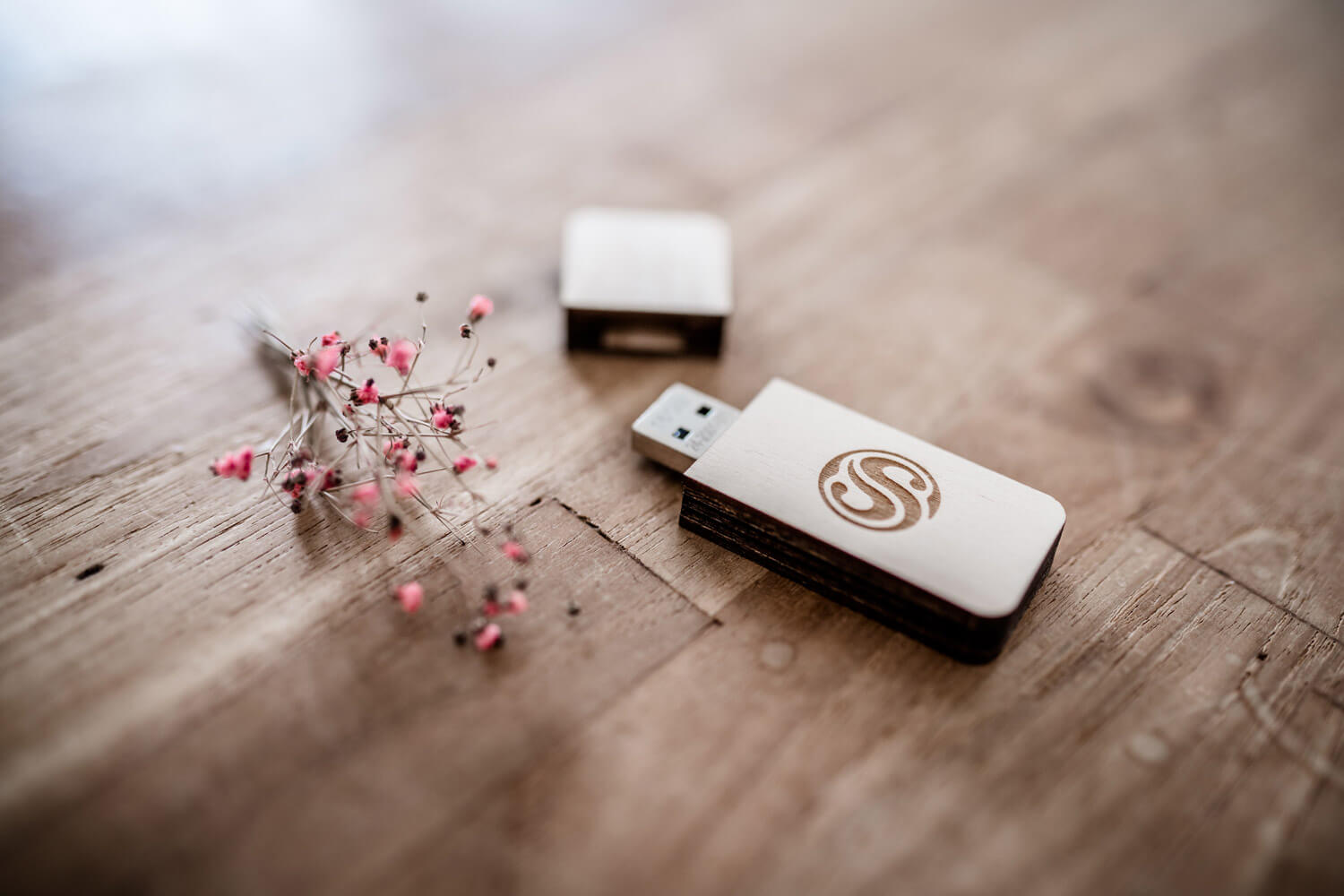 USB-Holzstick von Julia Schlenkrich Fotografie liegt auf Holztisch mit Blümchen