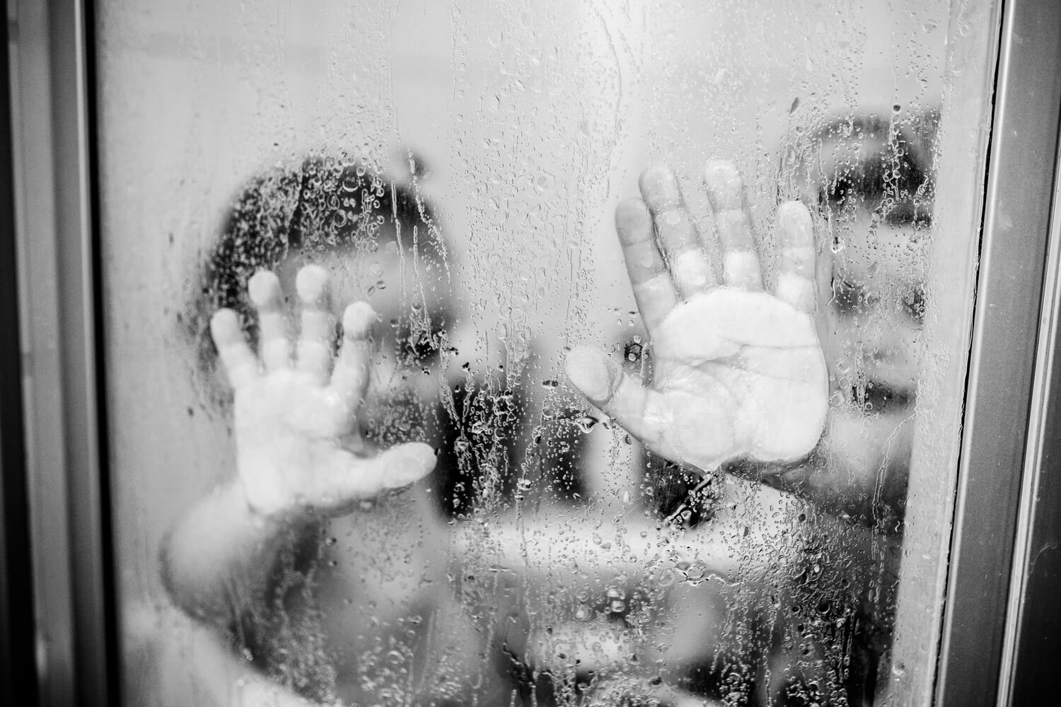 Nahaufnahme Kinderhand an Duschscheibe mit Wassertropfen, schwarzweiß