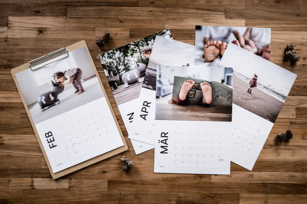 Flatlay einzelne Seiten des Fotokalenders 2023 ausgedruckt und mit Fotoabzügen bestückt, Kinderfotos