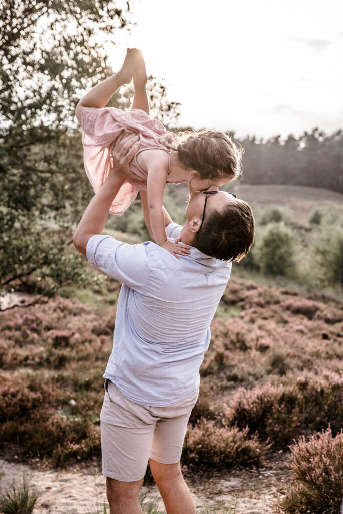 Papa hebt seine Tochter in die Luft, küsst sie dabei auf die Schläfte, Fotograf in der Nähe finden