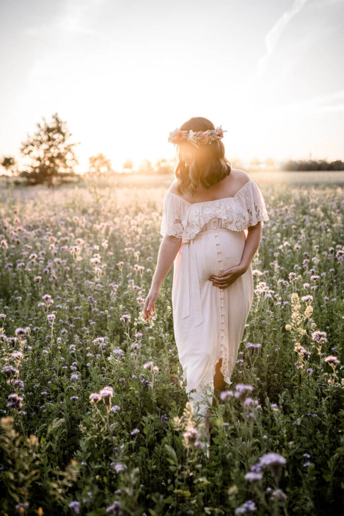 Schwangere Mama läuft in langem Kleid in einem Kornblumenfeld entlang, Sonnenuntergang, Babybauchshooting Kleid leihen