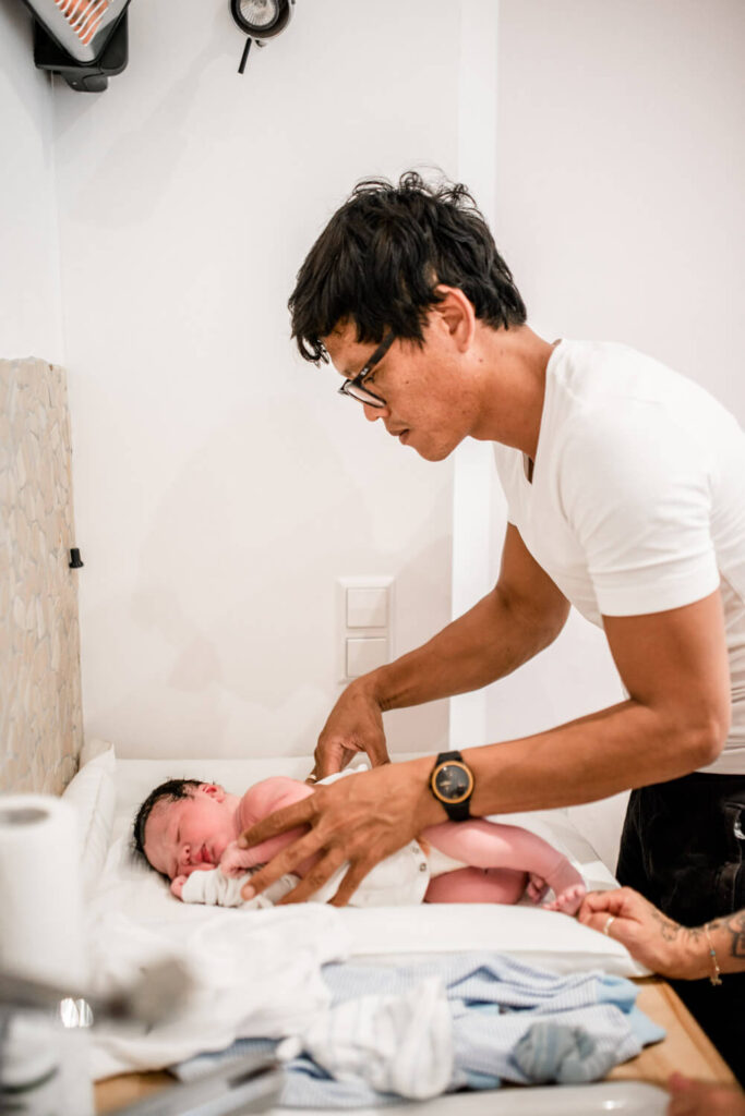 Vater zieht gerade geborenes Baby Kleidung auf Wickeltisch im Geburtshaus an, geburtsfotos