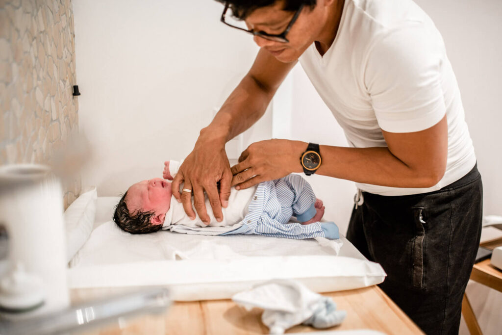 Vater zieht gerade geborenes Baby Kleidung an, geburtsfotos im geburtshaus