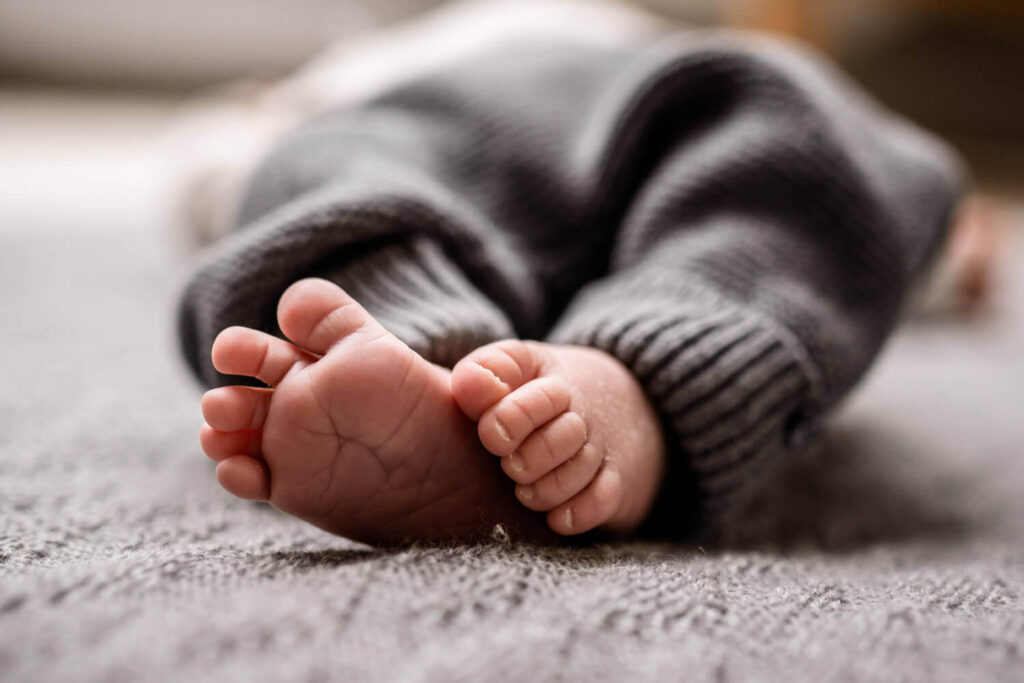 Detailaufnahme nackte Babyfüßchen liegen auf grauer Decke, newborn shooting wann buchen, Julia Schlenkrich Fotografie