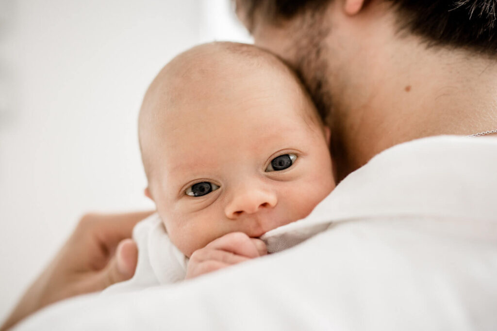 Waches Baby schaut über die Schulter des Vaters während Neugeborenen Shooting mit Julia Schlenkrich