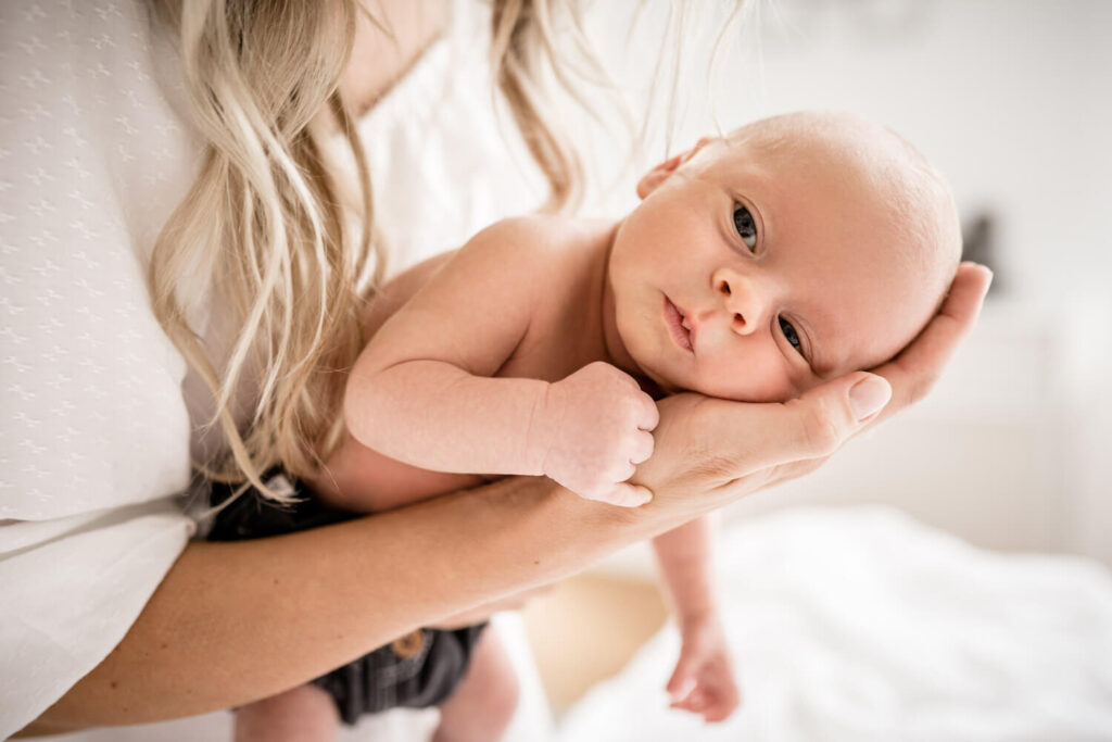 Waches Baby liegt auf der Hand der Mutter während eines Neugeborenen Shootings mit Julia Schlenkrich Fotografie