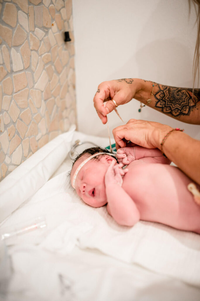 Hebamme untersucht ein gerade geborenes Baby, misst den Kopfumfang