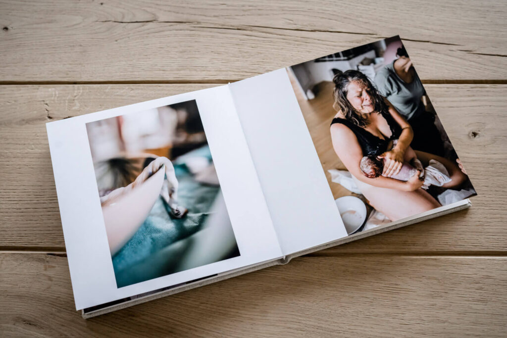 Geöffnetes Fotobuch mit Leineneinband liegt auf Holztisch, Bilder einer Geburtsreportage, Was kostet ein Geburtsfotograf