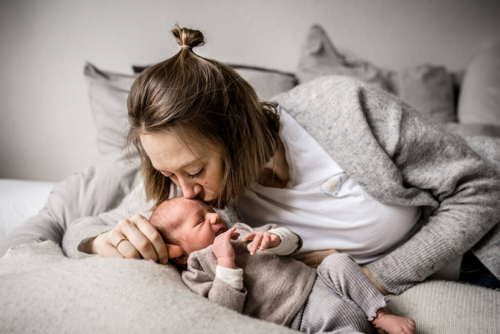 Mutter liegt mit ihrem neugeborenen Sohn auf dem Bett, sie küsst es auf den Kopf, newborn shooting hannover, wohnung ordentlich und aufgeräumt
